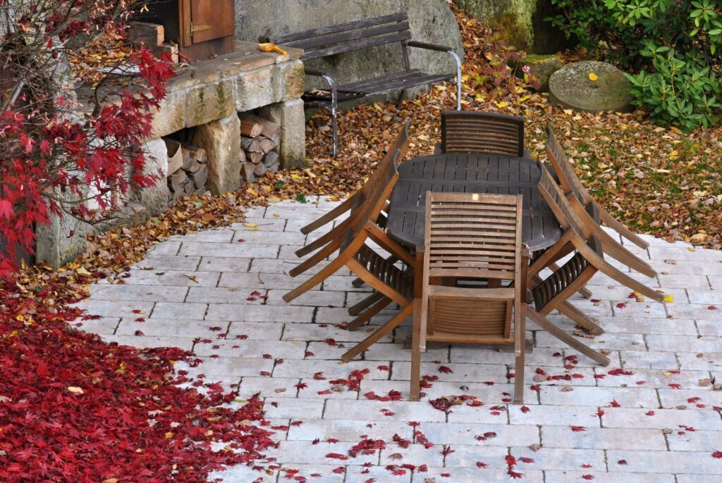Ein Gartentisch steht inmitten von Blättern, die sich im Herbst von den Bäumen gelöst haben.