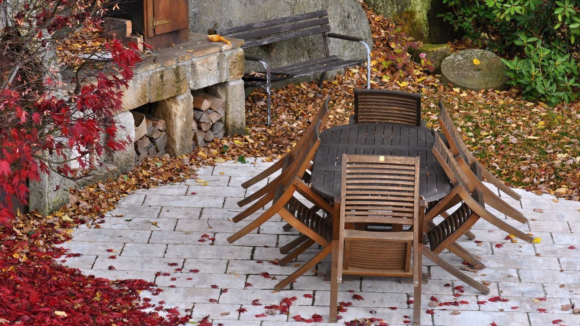 Ein Gartentisch steht inmitten von Blättern, die sich im Herbst von den Bäumen gelöst haben.