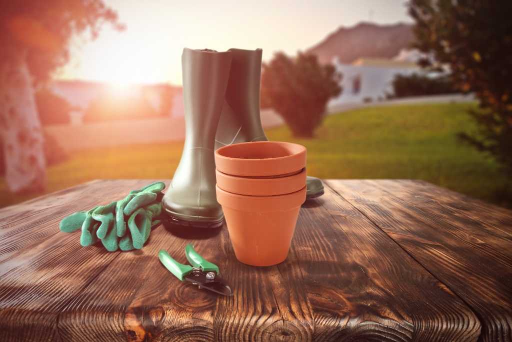 Gartenschuhe mit Blumentöpfen und Gartenzubehör auf einem Tisch im Garten.