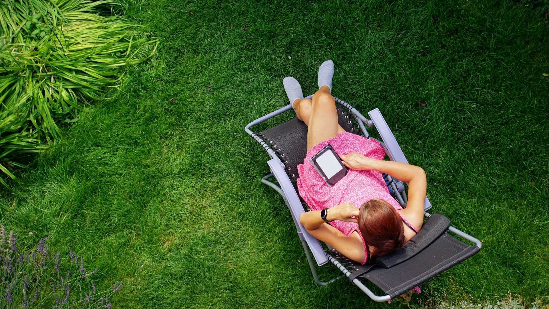 Liegestuhl im Garten, Frau sitzt darauf und liest ein eBook.