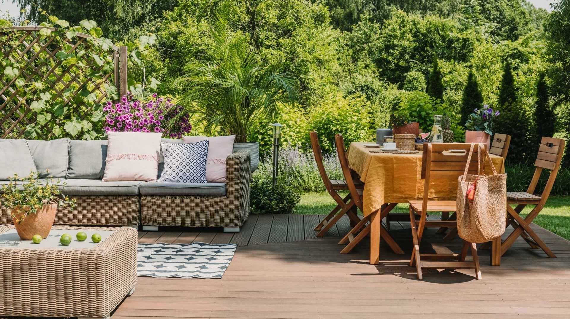Gartenmöbel auf einer Terrasse, Sitzlandschaft aus Rattanmöbeln mit einer Sofa Lounge und einem Holz Esstisch inmitten der grünen Natur