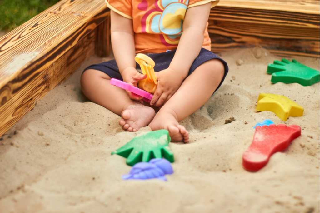 Ein Sandkasten mit Holzrahmen, feinem Sand und einem spielenden Kind
