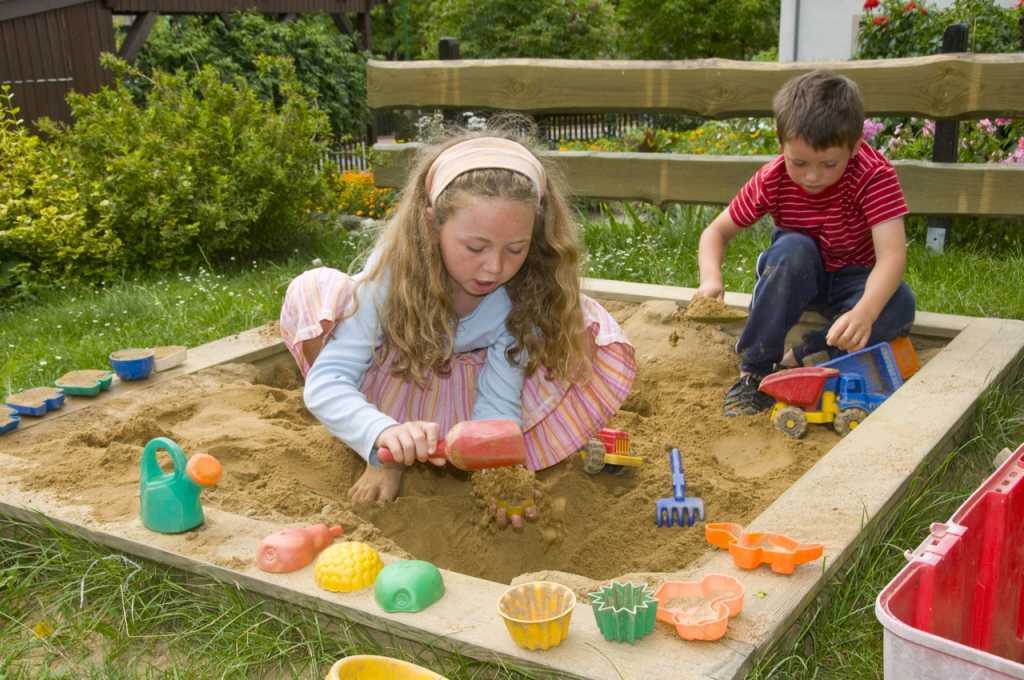 Zwei Kinder spielen in einem Sandkasten aus Holz