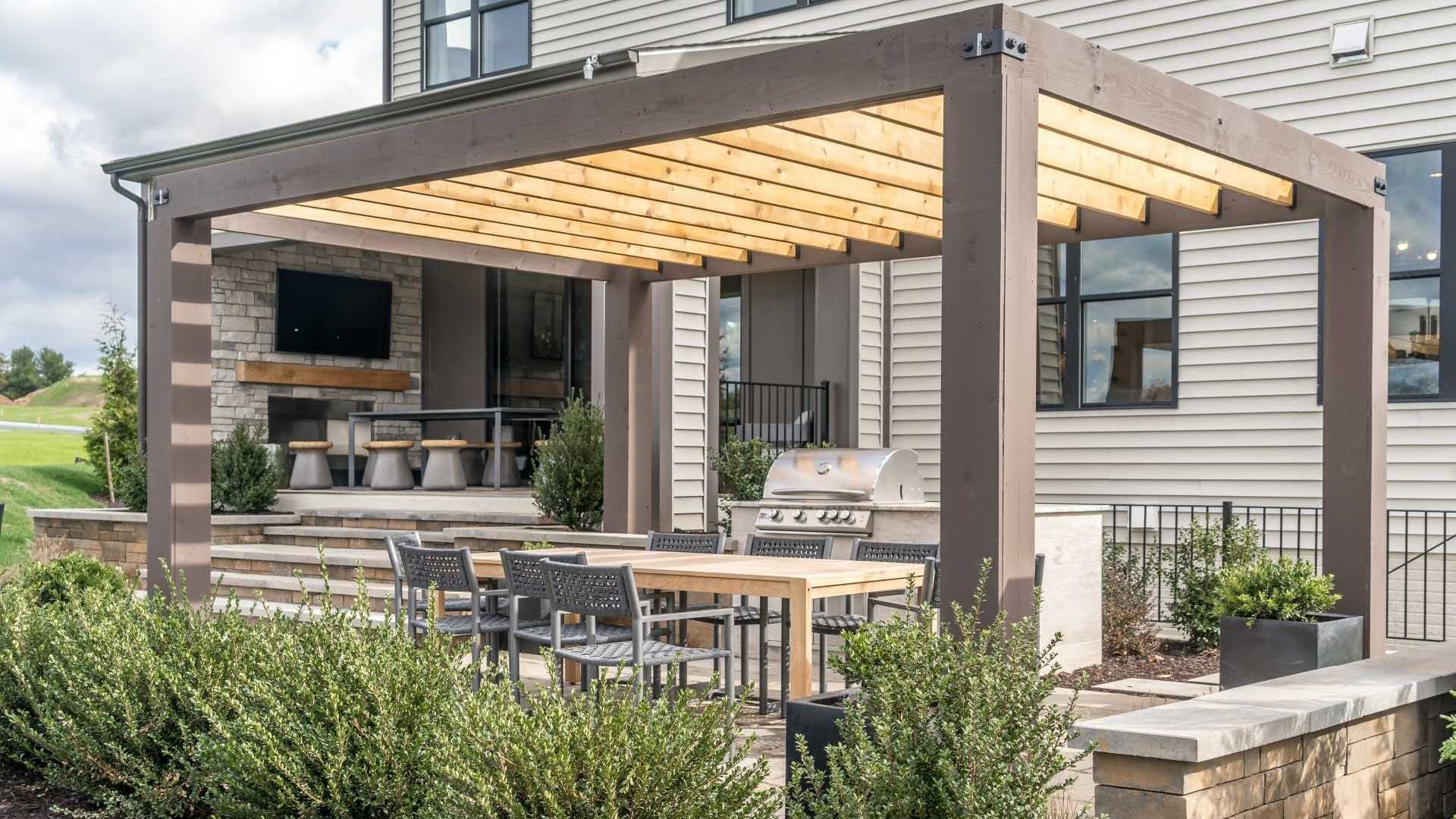 Terrassenüberdachung aus Holz und Metall im Garten. Darunter befindet sich eine gemütliche Sitzecke mit Grill.