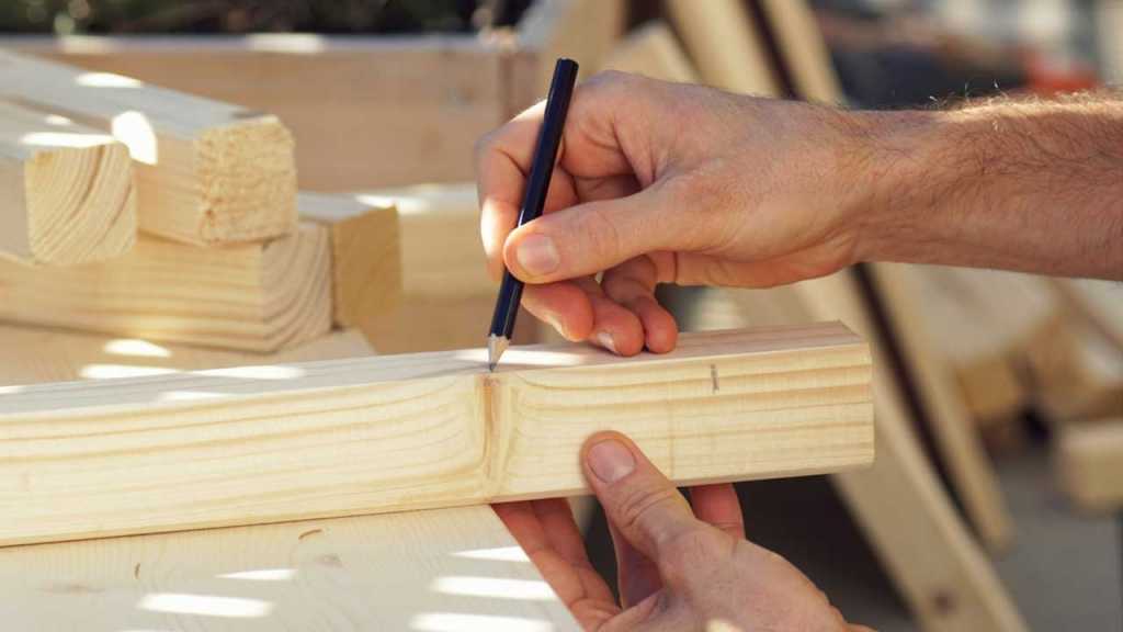 Mann misst ein Sück Holz