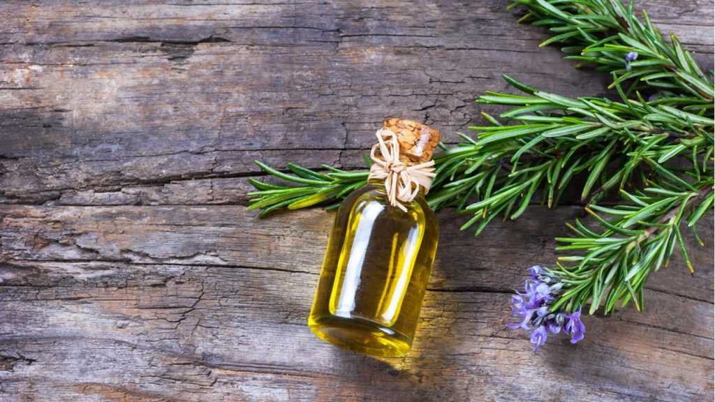 Rosmarin und eine kleine Glasflasche Öl liegen auf einem Holztisch