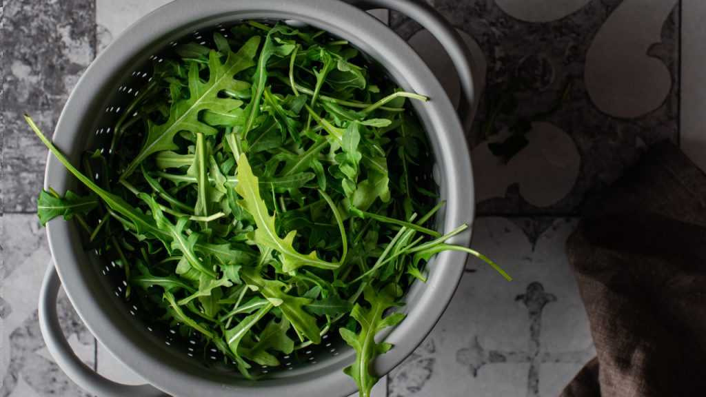 Ein Sieb voller Rucola steht auf einem Fliesenboden