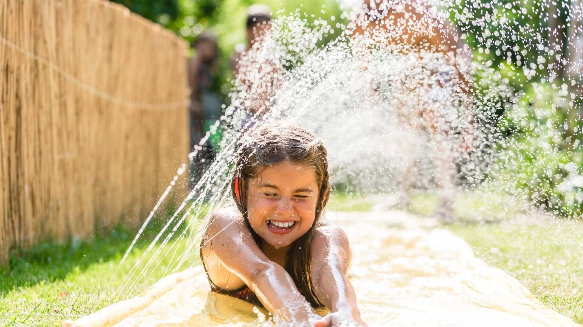 Mädchen rutscht Wasserutsche im Garten hinunter